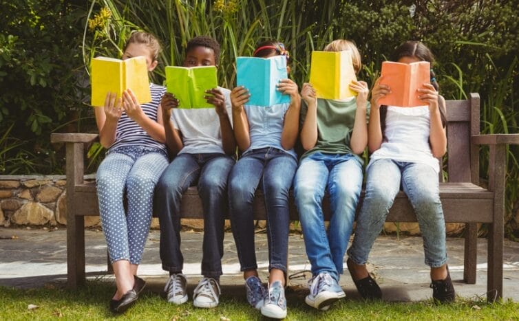 Студенты сидят на скамейке и читают, их лица в основном закрыты книгами.