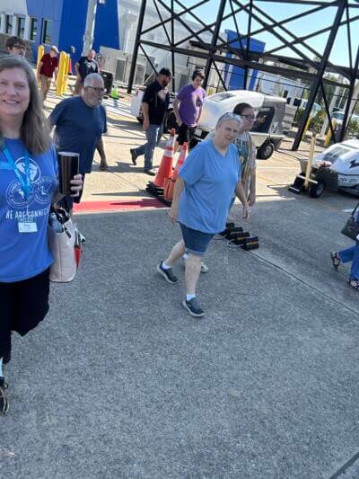 Группа людей гуляет на улице в солнечный день в окружении промышленных сооружений.