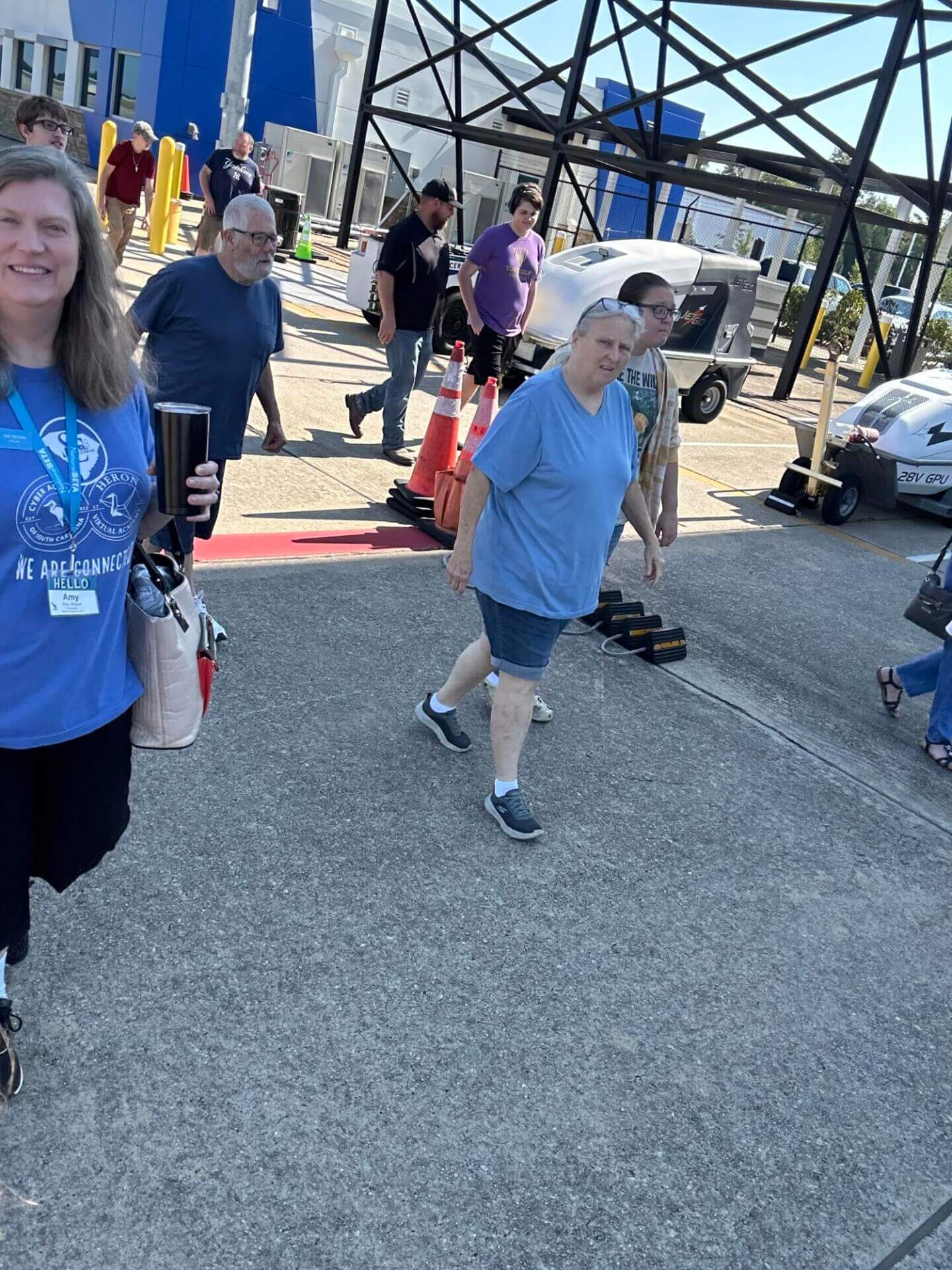 Группа людей гуляет на улице в солнечный день в окружении промышленных сооружений.