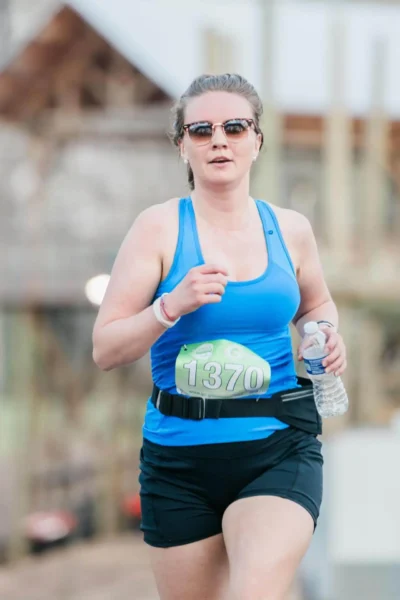 Женщина в очках бежит с бутылкой воды в руке