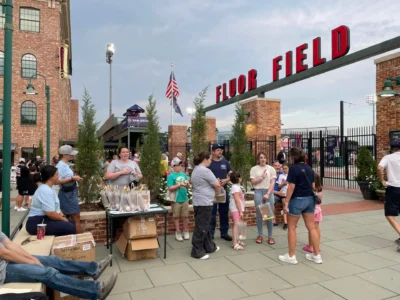 Разнообразная группа людей собралась у входа на поле Fluor Field, наслаждаясь обычным мероприятием на открытом воздухе.
