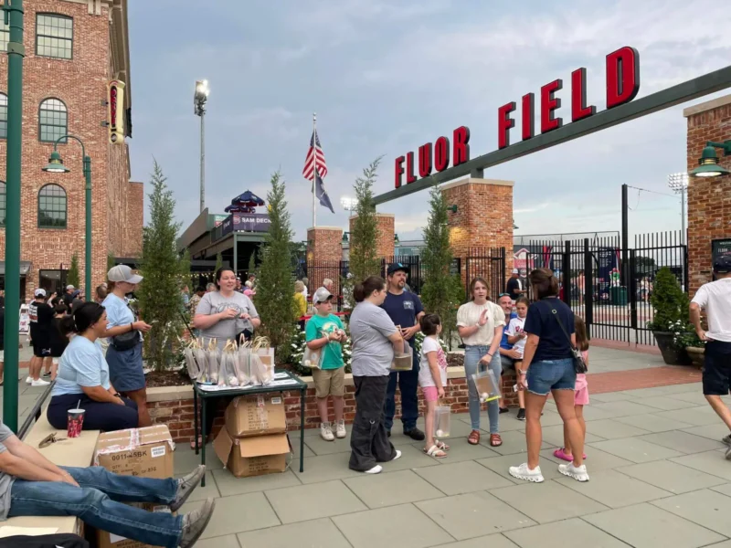 Разнообразная группа людей собралась у входа на поле Fluor Field, наслаждаясь обычным мероприятием на открытом воздухе.